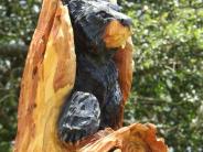 A close up of a chainsaw carving of a black bear emerging from the top of a tree